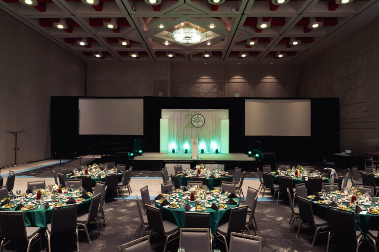 Ballroom set for a conference banquet at the CCF 2026 Annual Conference at the Salt Palace Convention Center, featuring a professionally designed stage, dual projection screens, and elegantly arranged guest tables.