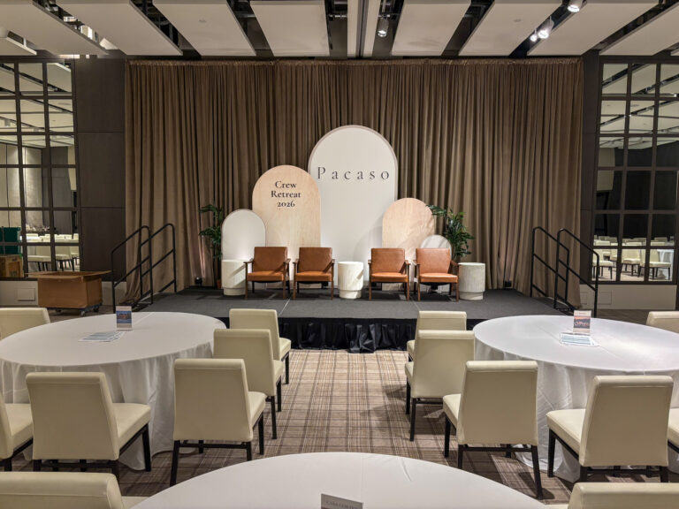 Custom stage design featuring branded arch backdrops, Dylan arm chairs, echo side tables, greenery, and event staging for the Pacaso Crew Retreat 2026, produced by In The Event.