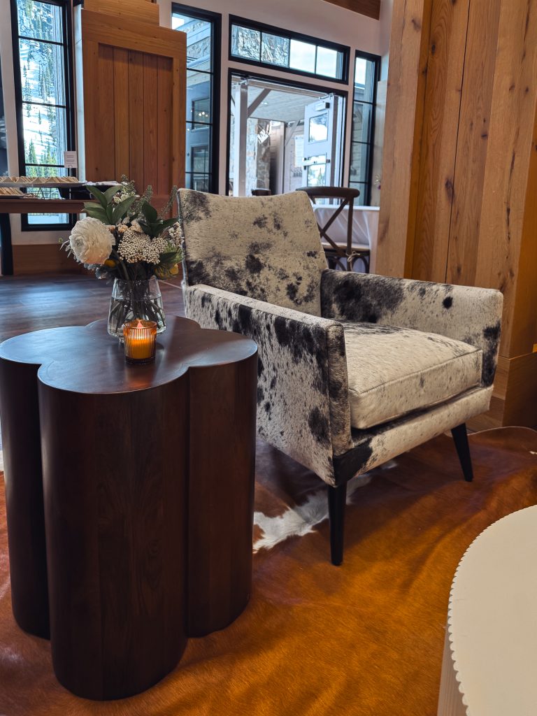 Cowhide upholstered lounge chair paired with a dark wood clover side table, floral arrangement, and candle.