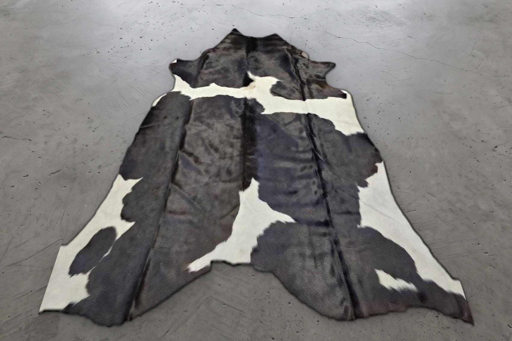 Black and white patched cowhide rug, approximately 7 feet, shown on a concrete floor