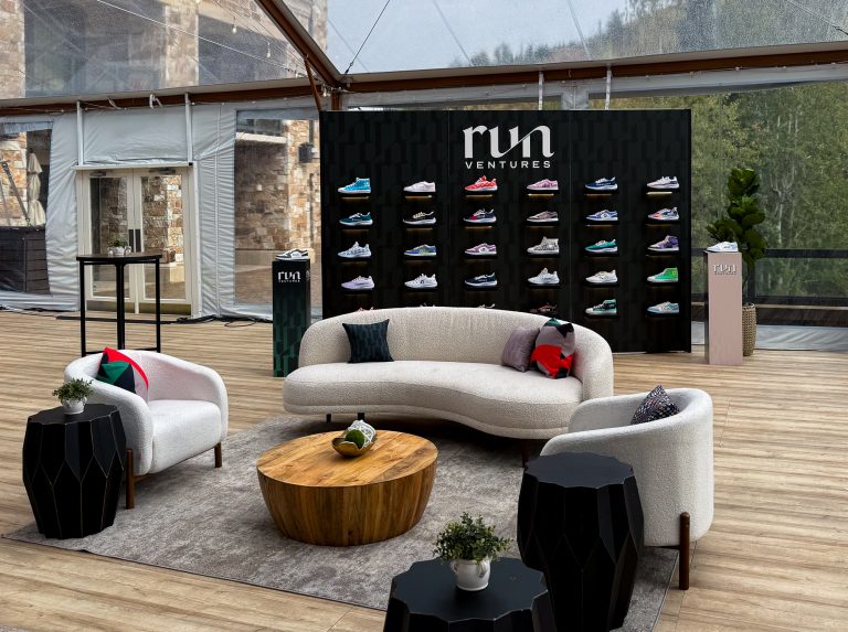 Run Ventures branded sneaker display wall behind a modern event lounge with curved white furniture, wood coffee table, and custom graphics at St. Regis Deer Valley.