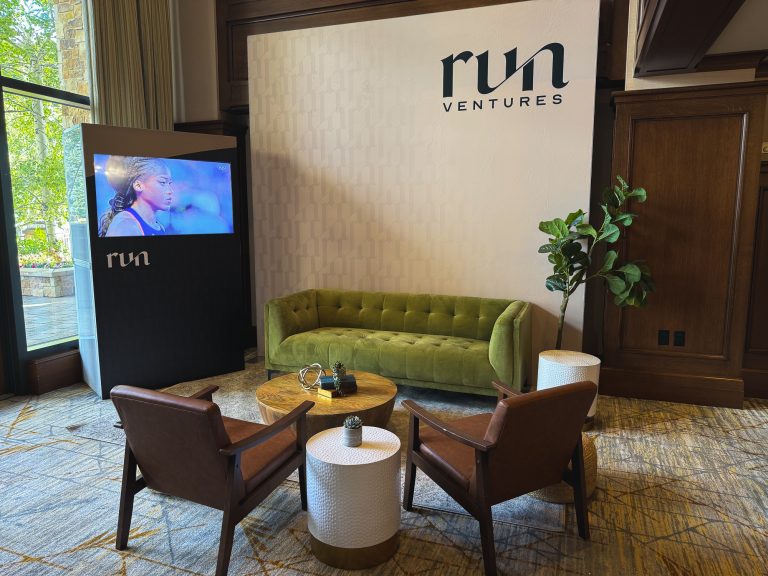 Run Ventures event lounge featuring a green tufted velvet sofa, brown leather chairs, wood coffee table, and custom branded backdrop with video display at St. Regis Deer Valley.