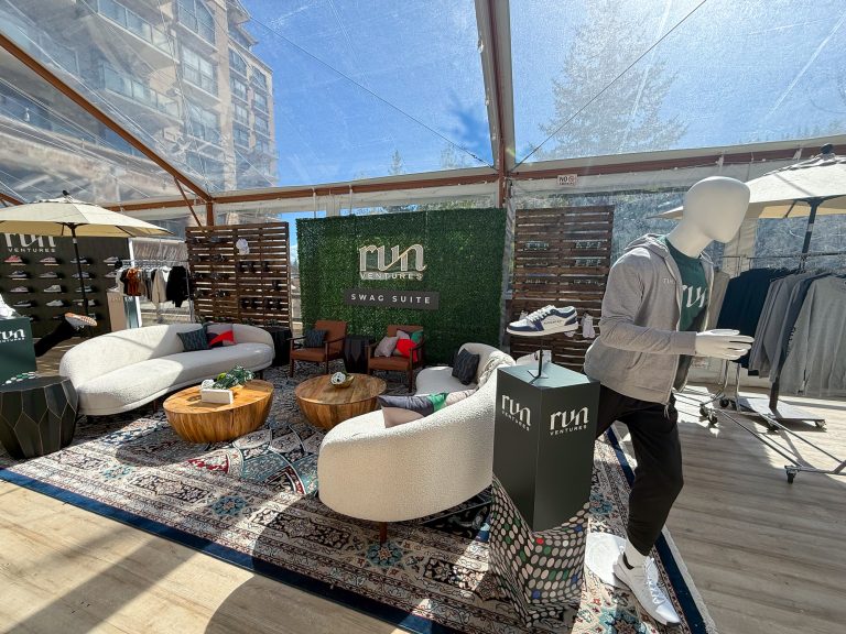 Run Ventures branded swag suite featuring curved white lounge sofas, wood coffee tables, custom sneaker displays, and apparel racks beneath a clear event tent at St. Regis Deer Valley.
