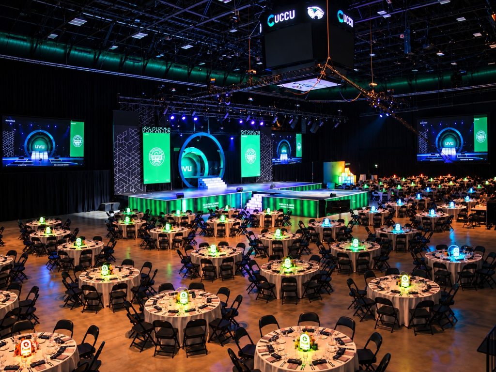 Wide view of the UCCU Center arena at the UVU President's Scholarship Ball 2026 with the portal stage, outboard screens, and lit centerpiece tables